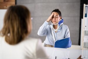 An injured woman wearing a neck brace and an arm sling, meeting with an experienced car accident lawyer in Long Beach.