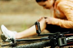 An injured female bicycle rider sits on the road next to her damaged bicycle. A bicycle accident lawyer in Riverside will help you claim damages.