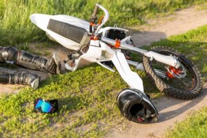 A rider lying next to his bike on a dirt road and sustaining motorcycle accident injuries.