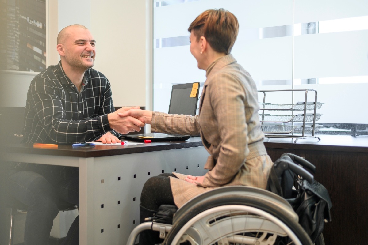 A woman in a wheelchair shaking hands with her personal injury lawyer.